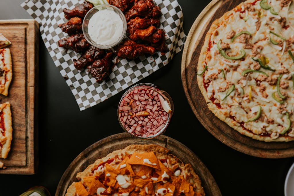 A mouthwatering spread of pizzas and chicken wings with a refreshing drink, perfect for sharing.