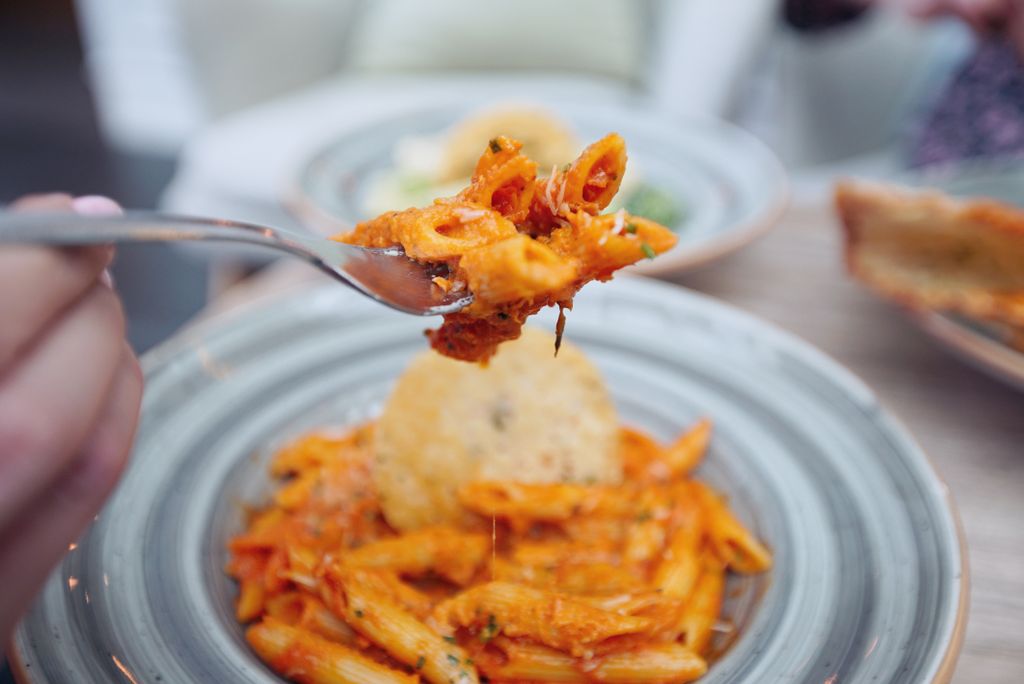 Fork lifting penne pasta in tomato sauce, highlighting rich textures and colors.